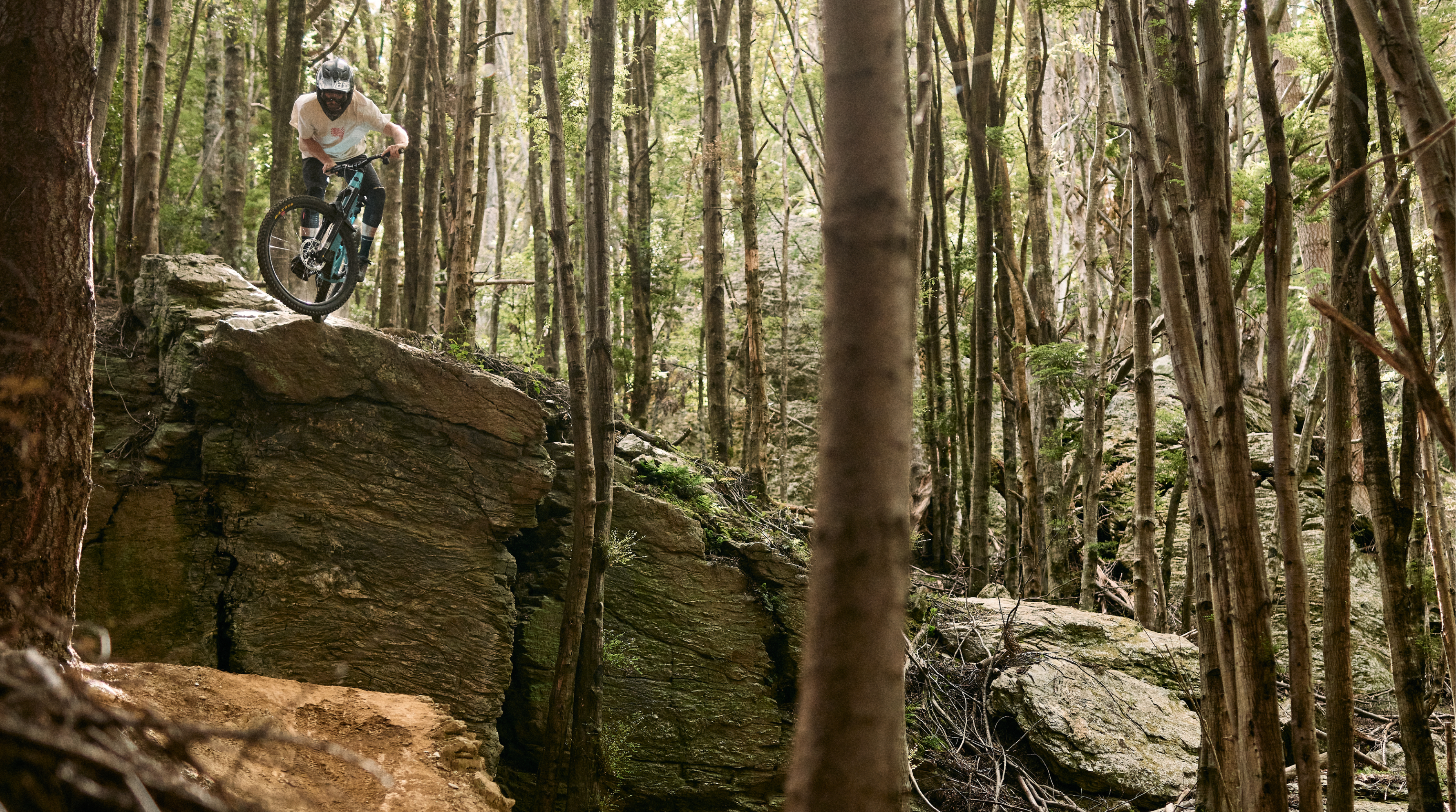 A mountain biker jumping off a rock feature in the woods. 