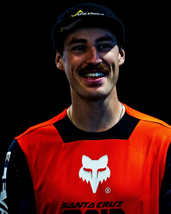 Andreas Kolb wearing an orange and black Syndicate Jersey with a logo on a blue background